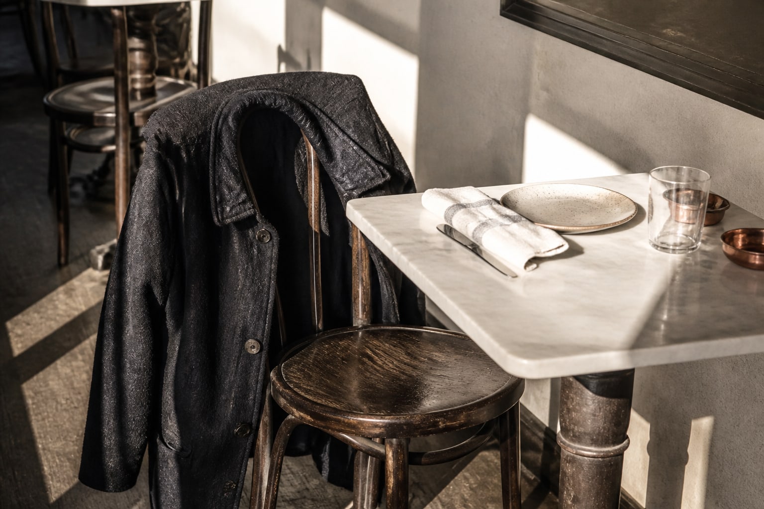 A dark wool coat draped over an empty restaurant chair