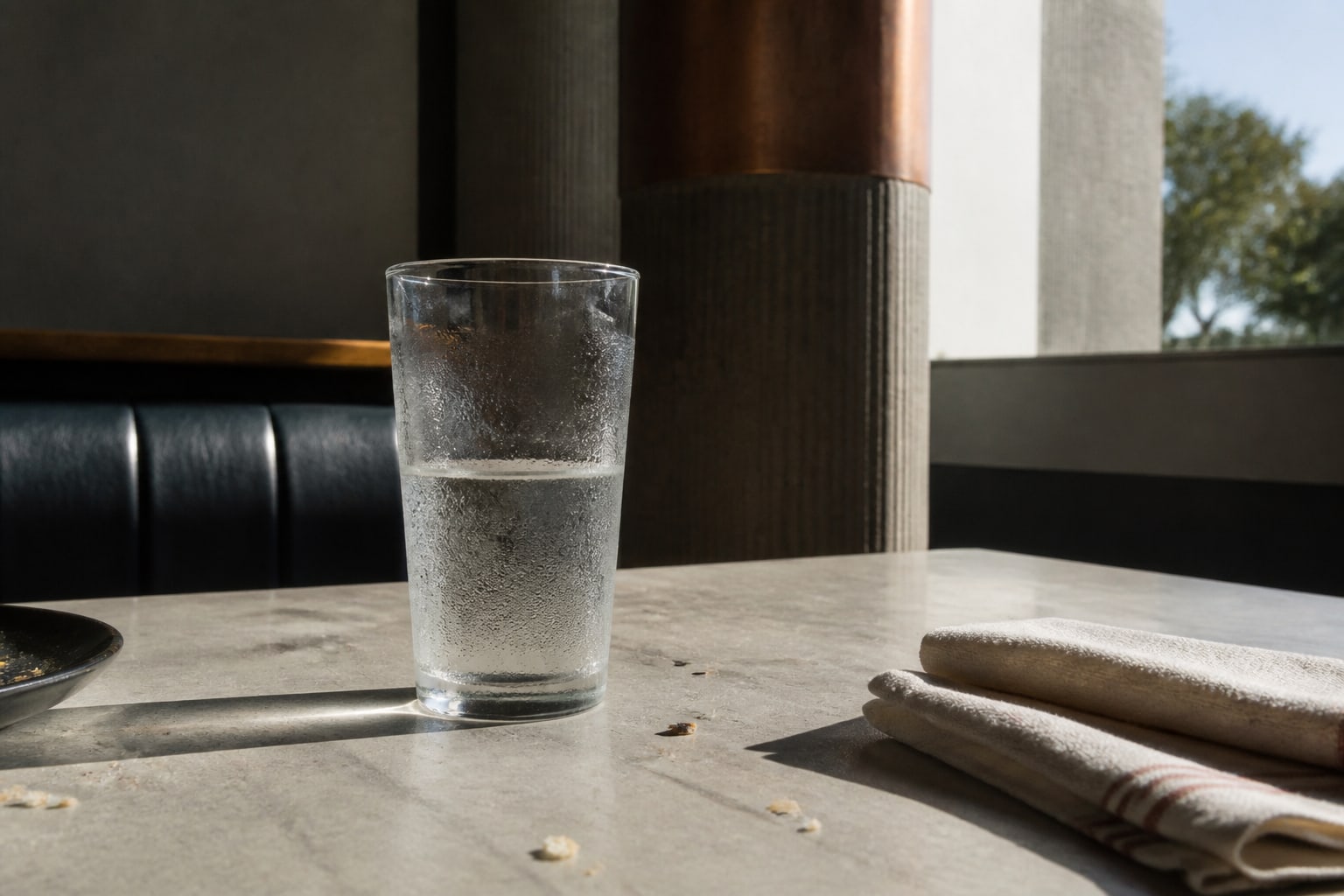 A condensation-covered water glass on an almost-cleared lunch table